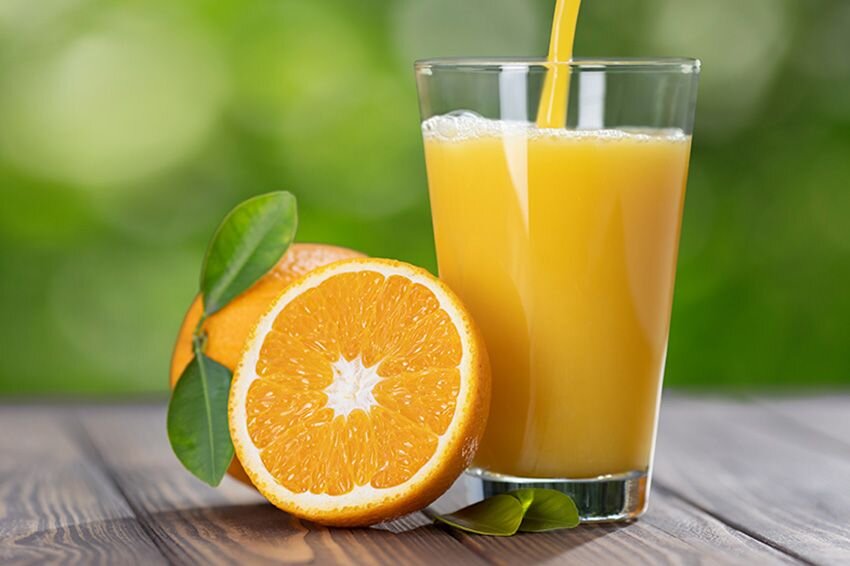 Jugo de naranja vertido en vaso y dos naranjas sobre una mesa. 